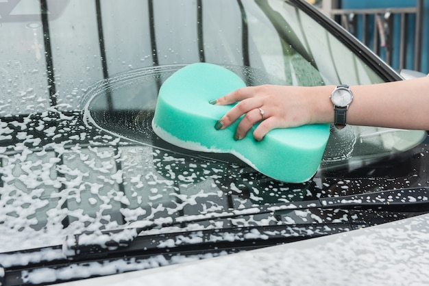 Auto di pulizia delle mani femminili in servizio con acqua e schiuma di sapone strumenti. lavare auto