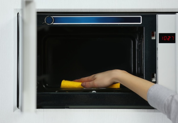 Female hand cleaning microwave with a sponge