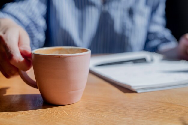 写真 ぼやけたノートと背景にペンでカフェでコーヒーカップを取る女性の手のクローズアップ