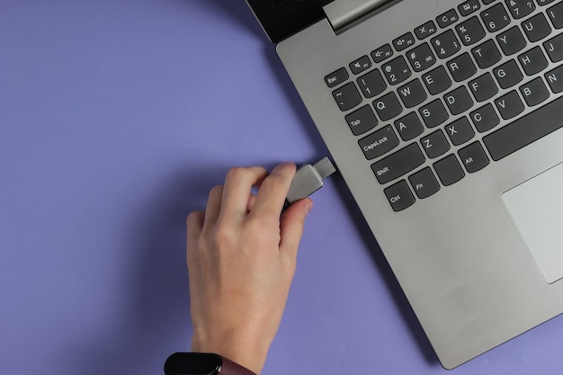 Фото Женская рука подключает флешку к ноутбуку на фиолетовой бумаге