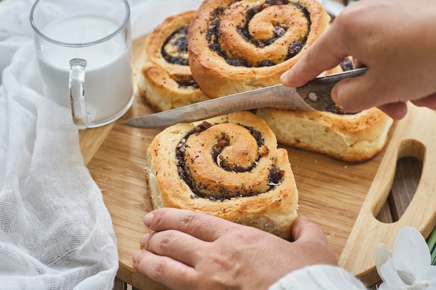 Female hand cut homemade buns with jam, served on old wooden table with walnuts and cup of milk