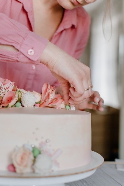 写真 スタンドにピンクの花の結婚式の誕生日ケーキを飾る女性の手。