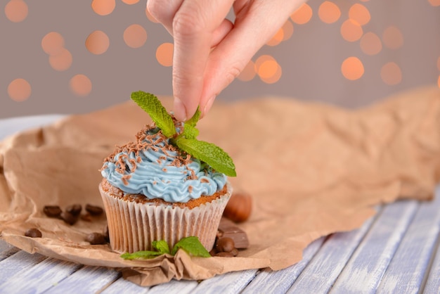 Photo female hand decorating tasty cupcake with butter cream on color wooden table on lights background