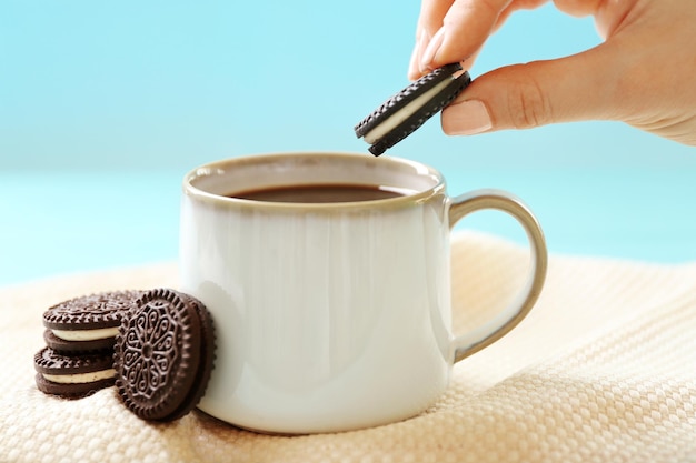 Female hand dipping chocolate cookie into cup of coffee close up view