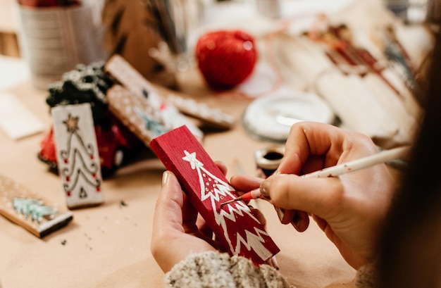 Female hand drawing a Christmas tree on a red-colored wooden stick