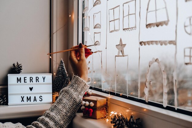 Foto la mano della donna disegna la decorazione delle vacanze di natale dipinta sul vetro della finestra