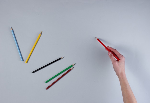 Female hand draws color pencil on gray surface. 