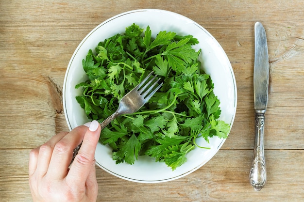 female hand eating green herbal salad from plateon old wooden table