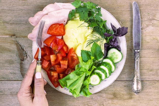 Female hand eating omlette with tomato cucumber herbs ham lettuce from plate on old wooden table