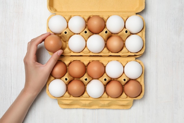 Female hand and egg boxes on white wooden background