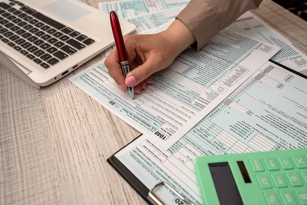 Female hand  filling US tax form 1040 with help calculator and laptop in the office