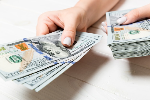 Female hand giving one hundred dollar banknotes on wooden table