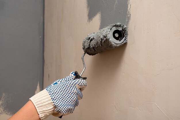 Foto la mano femminile in un guanto dipinge il muro con un cuscino a casa. avvicinamento.