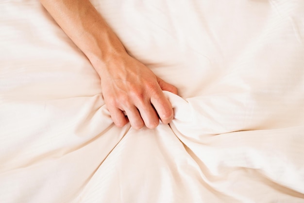 Female hand grasping on white bed sign of woman orgasm