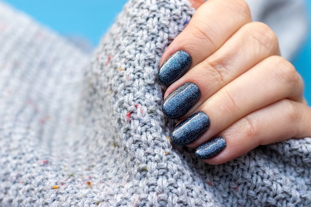 Female hand in gray knitted sweater fabric with blue glittered nails