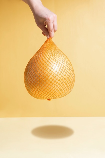 Female hand hangs yellow fresh pomelo in mesh packaging, close up.