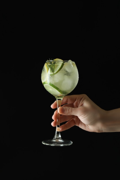 Female hand hold glass of cocktail with citrus on dark surface