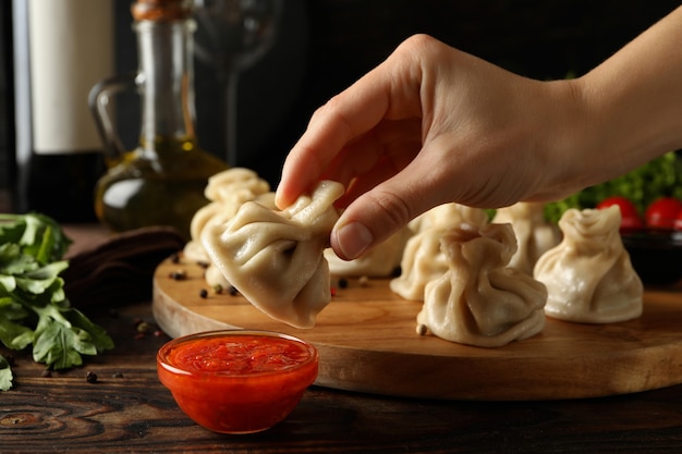 Female hand hold khinkali over the sauce on wooden table with khinkali