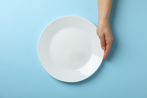 Female hand hold plate on blue background, top view