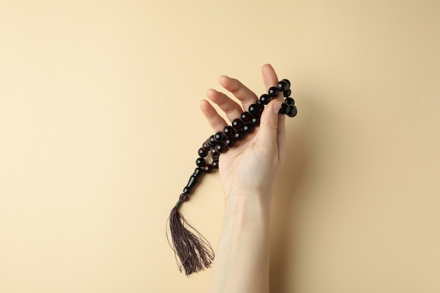 Female hand hold prayer beads on beige surface