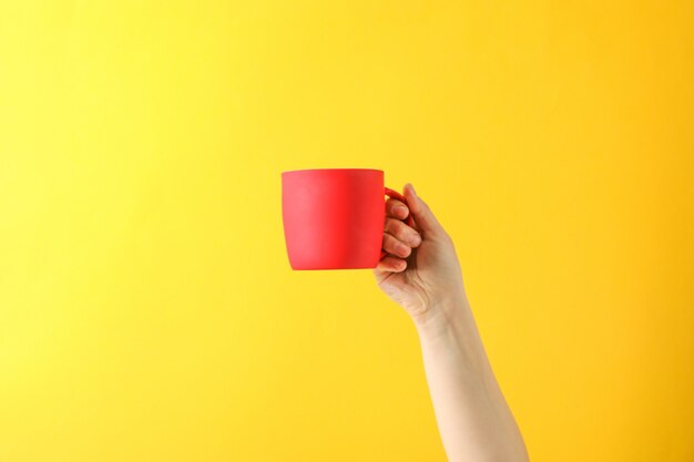 Female hand hold red cup against color background