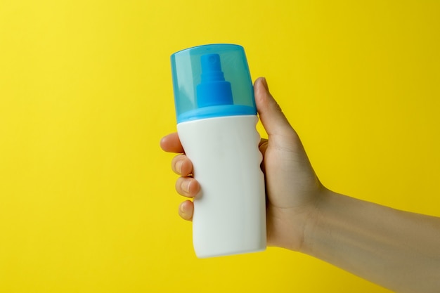 Female hand hold sunscreen on yellow