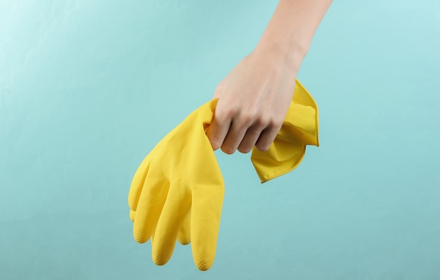 Female hand hold yellow gloves for cleaning on blue background. Home cleaning concept