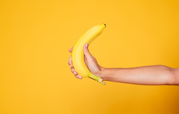 female hand holding banana fruit nutrition concept human hand holding a banana isolated on orange background
