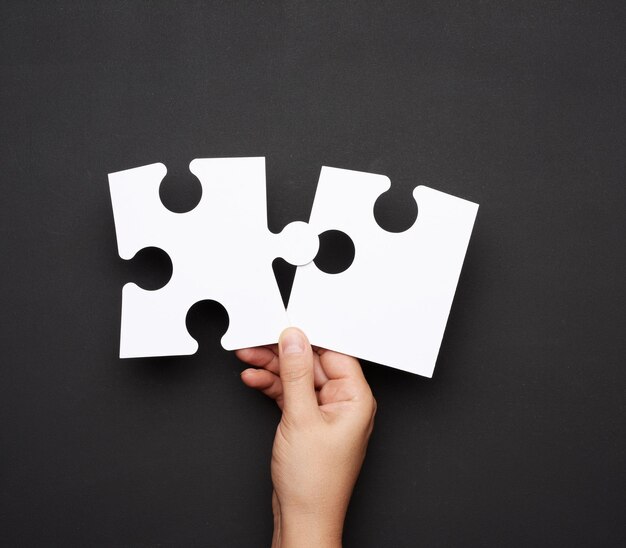 Foto mano femminile che tiene un grande puzzle bianco su uno sfondo nero concetto di business