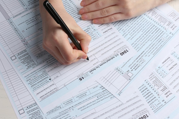 Female hand holding a black pen and filling in the 1040 Individual Income Tax Return Form for 2015 year on the white desk close up