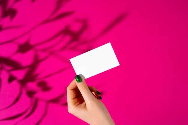 Female hand holding blank businesscard. Creative photo with shadow