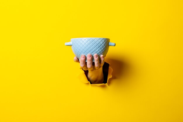 Female hand holding a blue bowl on a bright yellow