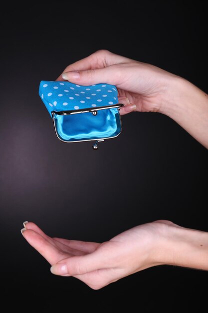 Female hand holding blue purse on black background