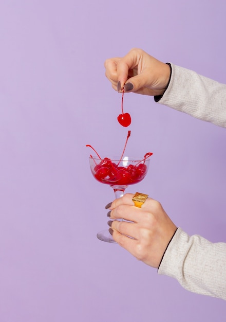 Female hand holding bowl with cherries. Lilac background.