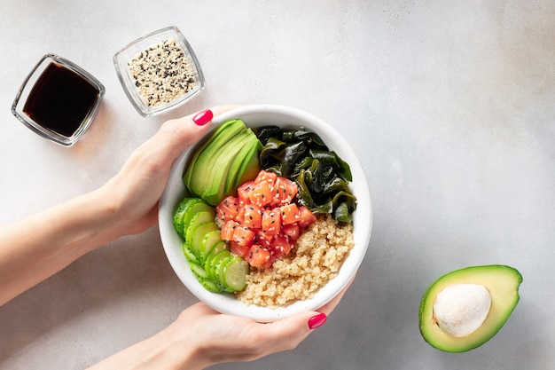 Female hand holding bowl with quinoa salmon avocado cucumber wakame seaweed healthy asian food