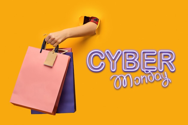 Female hand holding bright shopping bags on yellow. Cyber monday and sale concept