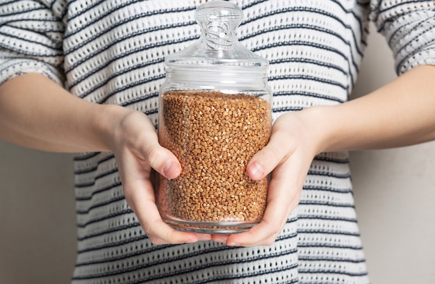 Female hand holding buckwheat in glass jar for storage. Closeup shot