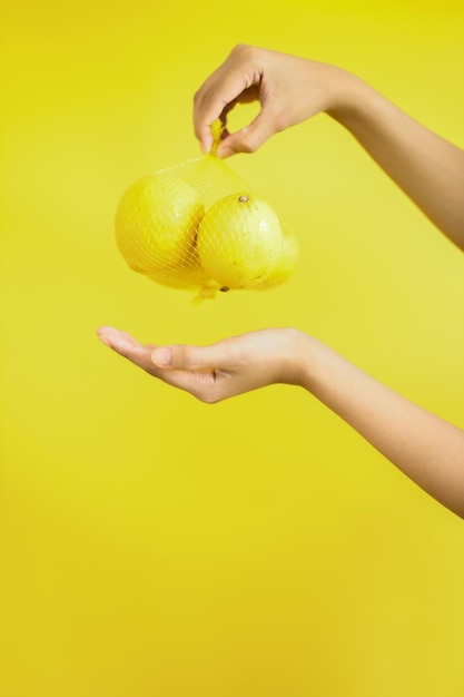 노란색 배경에 레몬 다발을 들고 있는 여성의 손 건강한 생활 방식과 영양 개념