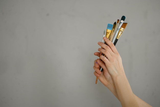灰色のセメントスタジオの壁に絵筆の束を持っている女性の手