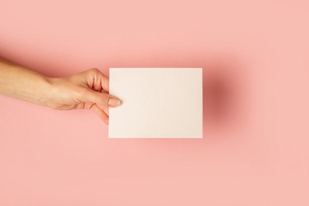 Female hand holding a card on a pastel pink surface