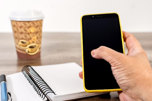 Female hand holding cell phone notebook and coffee cup on wooden table