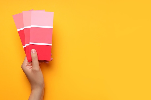 Female hand holding color palettes on yellow background