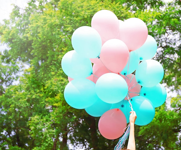 Female hand holding colorful balloons in green park