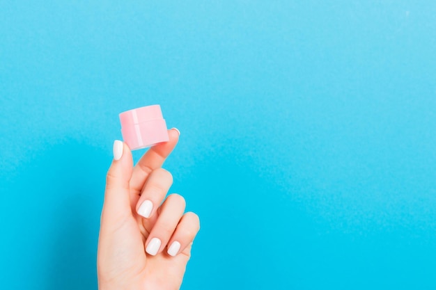 Female hand holding cream bottle of lotion isolated Girl give jar cosmetic products on blue background