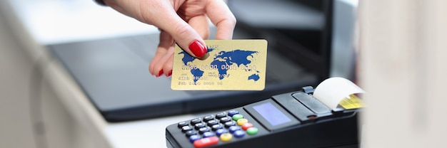 Female hand holding credit bank card near pos terminal closeup.