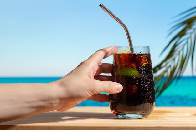 Female hand holding Cuba Libre cocktail at summer beach bar