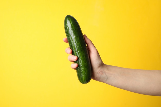 Female hand holding cucumber on yellow surface