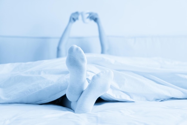 Female hand holding cup of coffee from under a blanket in bed Woman waking up in the morning