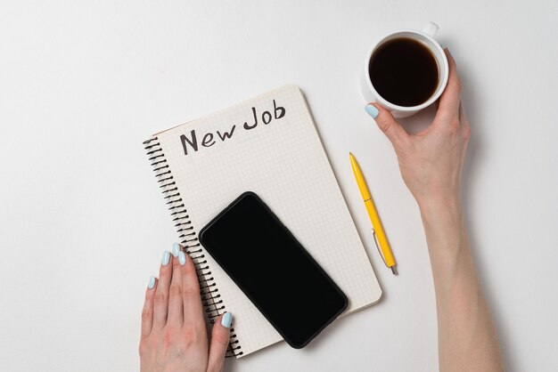 Female hand holding a cup of coffee Notebook and smartphone on white background New job Copy space