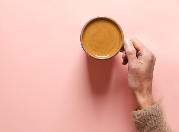 Female hand holding a cup of coffee on a pink background Flat lay top view